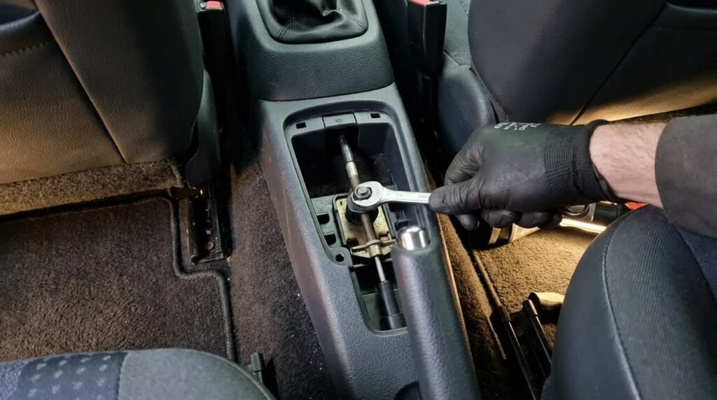Mécanicien serrant l'écrou de tension du câble de stationnement sous le cendrier d'une Renault Clio II