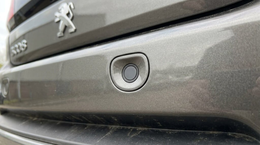 Gros plan sur l'un des capteurs ronds du radar de recul intégré dans le pare-choc arrière d'une Peugeot 3008.
