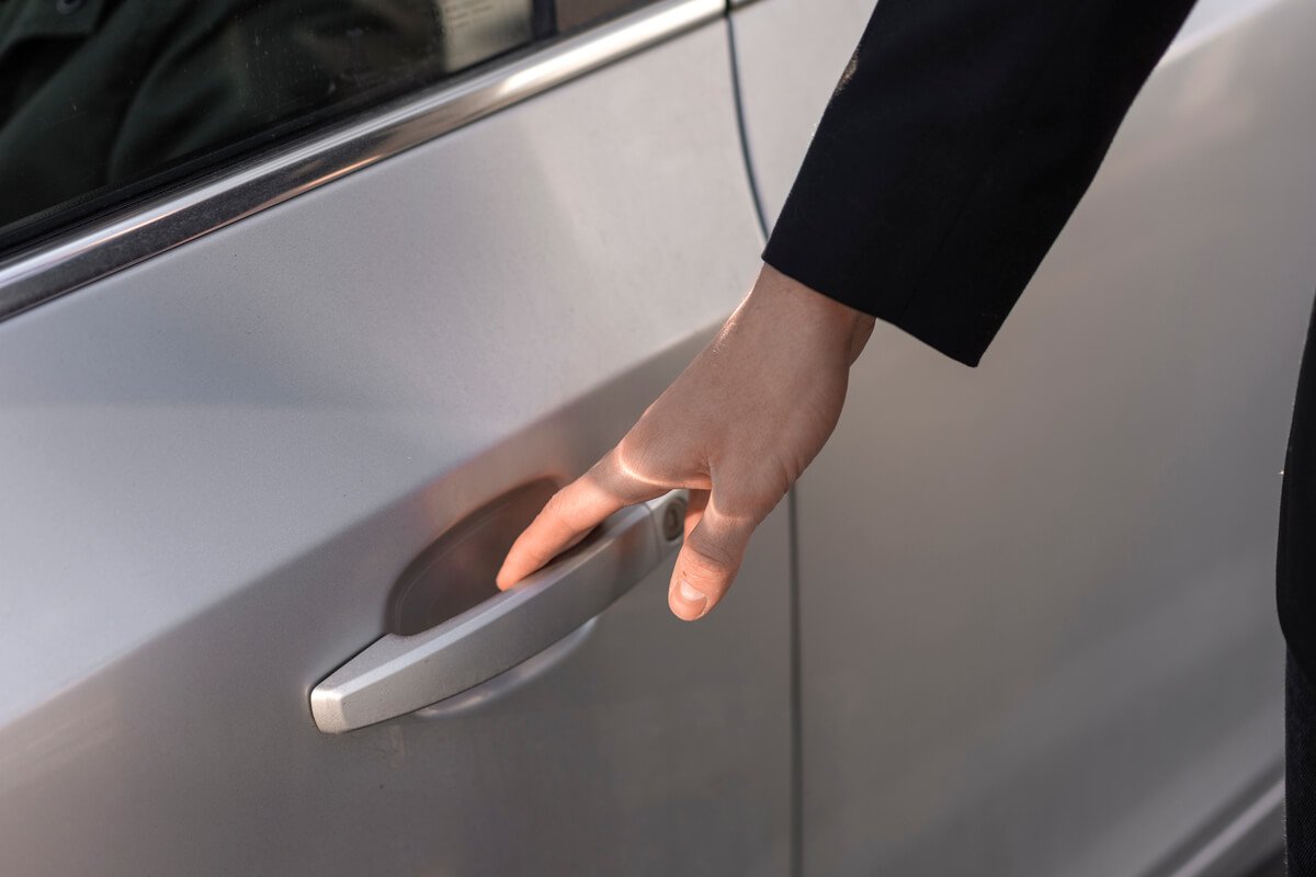 Une main touchant la poignée métallique d'une portière de voiture.