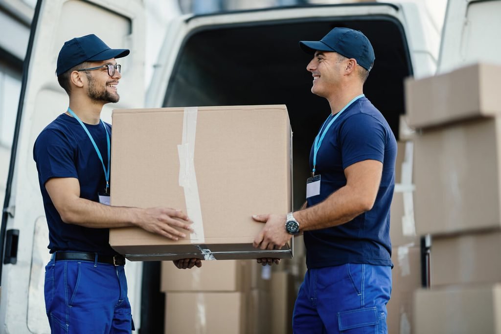 Déménagement : comment bien préparer son changement de logement ? 3 Déménageurs chargeant des meubles et des cartons à l'arrière d'un camion utilitaire.